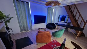 Ein modernes Wohnzimmer mit Holzboden, einem roten Tisch mit Flasche und Gläsern, einem grünen Sessel und einem schwarzen Sitzsack.