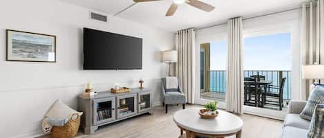Un salon moderne doté d’un téléviseur à écran plat, d’un ventilateur de plafond, d’un coin repas avec une table et des chaises, et d’un balcon offrant une vue agréable.