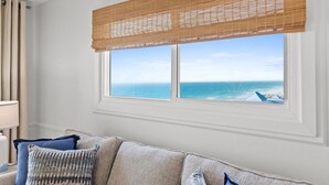 A room with a large window overlooking the ocean, a beige sofa with patterned cushions, and a white lamp on a side table. - Gulffront Condo w/ Tiki Bar, Pools, & Sunsets (Panama City Beach)