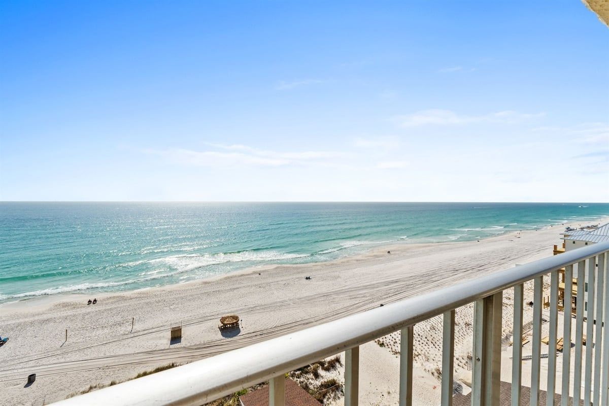 Blick auf einen Strand vom Balkon mit Geländer, feinem Sand und dem Meer.