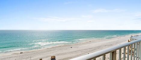 Blick auf einen Strand vom Balkon mit Geländer, feinem Sand und dem Meer.