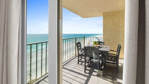 A balcony with a table and chairs, overlooking a beach and the ocean. - Gulffront Condo w/ Tiki Bar, Pools, & Sunsets (Panama City Beach)