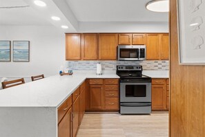 A modern kitchen with wooden cabinets, a stainless steel oven, and a microwave. - Gulffront Condo w/ Tiki Bar, Pools, & Sunsets (Panama City Beach)