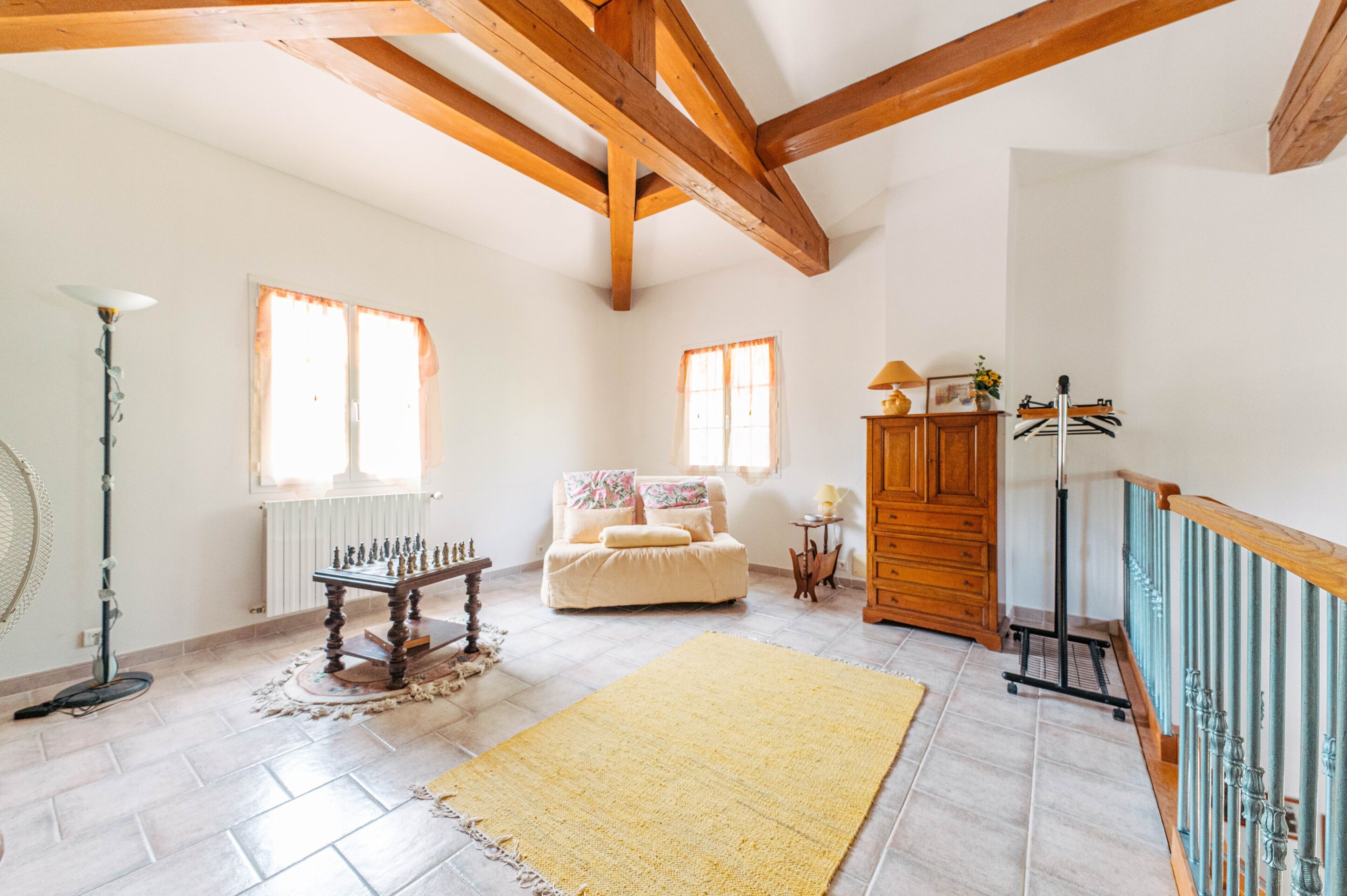 Una habitació àmplia amb sostre alt, bigues de fusta, un sofà, una taula i un radiador.