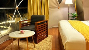 Ein gemütliches Zimmer mit einem Bett, einem Sessel, einem kleinen Tisch und einem Fenster mit Vorhängen.