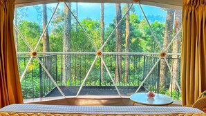 Eine Zeltdominierung mit Bett, Blick auf einen Wald durch ein Fenster und ein Balkon mit Geländer.