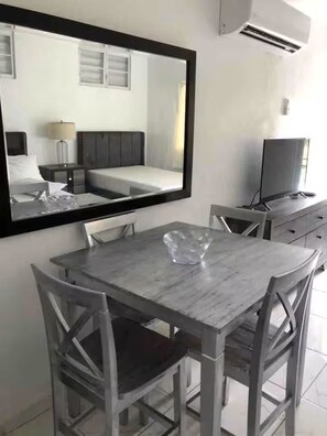 A hotel room with a bed, bedside table, lamp, TV, and a dining area with a table and chairs.