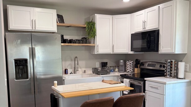 Una cocina moderna con gabinetes blancos, electrodomésticos de acero inoxidable, una isla de madera y dos taburetes de bar.