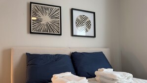 Una cama bien hecha con una cubierta blanca acolchada, dos almohadas azul marino y dos toallas blancas dobladas sobre la cama.
