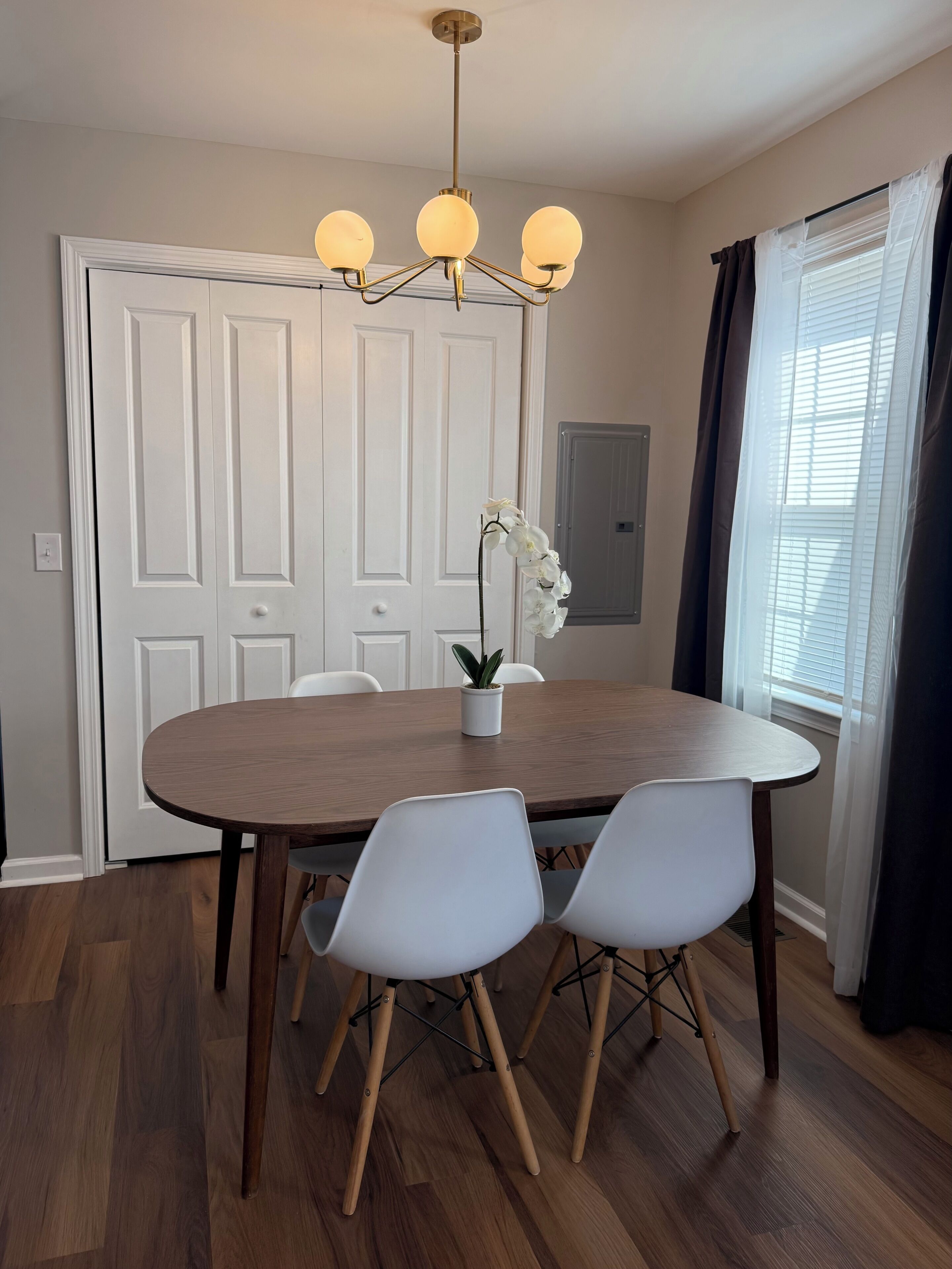 Un coin repas avec une table ronde en bois, des chaises blanches, un lustre et une orchidée en pot.