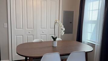 Un coin repas avec une table ronde en bois, des chaises blanches, un lustre et une orchidée en pot.