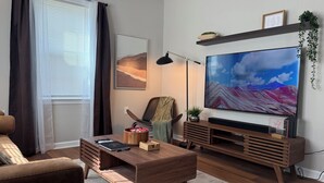 Una sala moderna con un televisor de pantalla plana grande, muebles de madera, una planta y un cuadro en la pared.