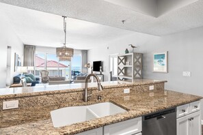 A modern kitchen with granite countertops, a stainless steel sink, and white cabinetry. - Tides 401 Corner Unit-Pool- Overlooks the Gulf! (Miramar Beach)