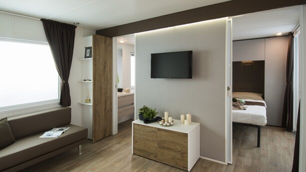 Una sala moderna con un sofá, una consola de madera con un televisor y una cama al fondo.