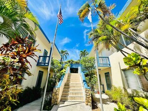 A hotel entrance with a staircase leading to a building, surrounded by palm trees and an American flag. - Charming studio condo with a coastal comfort (Christiansted)