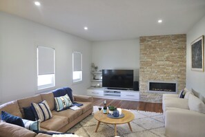 Een moderne woonkamer met een beige bank, een salontafel, een flatscreen-televisie en een stenen open haard.