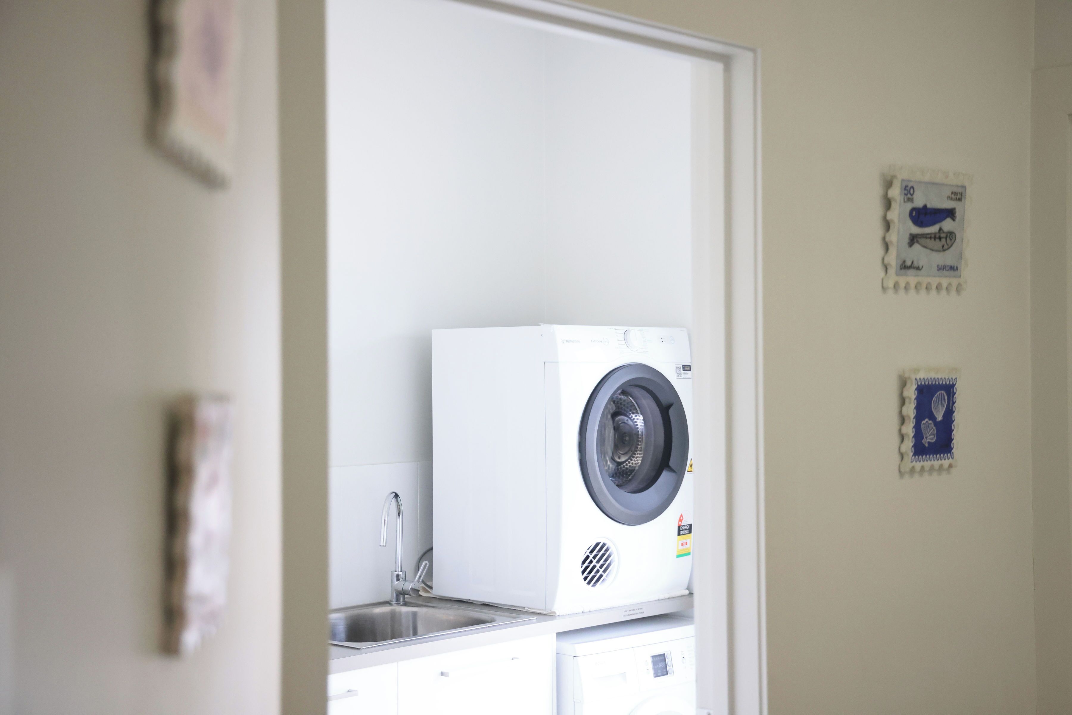 Une buanderie équipée d’un lave-linge et d’un sèche-linge, d’un évier et de deux timbres-poste accrochés au mur.
