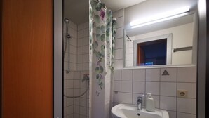 Een badkamer met een douche, een wastafel en een spiegel.