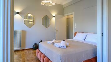 A hotel room with a large bed, two wall-mounted light fixtures, a radiator, and a door leading to another room.