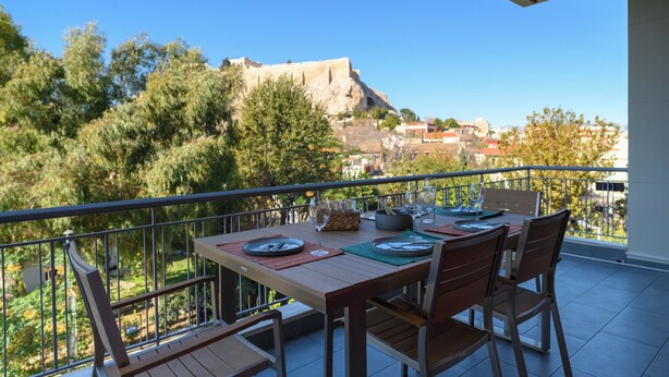 Un balcón con mesa dispuesta para comer, con vistas a una colina y una estructura que recuerda a una fortaleza.