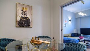 Una camera moderna con un tavolo in vetro, poltrone rivestite di blu, un quadro raffigurante un cane con una corona e un letto con copriletto blu.