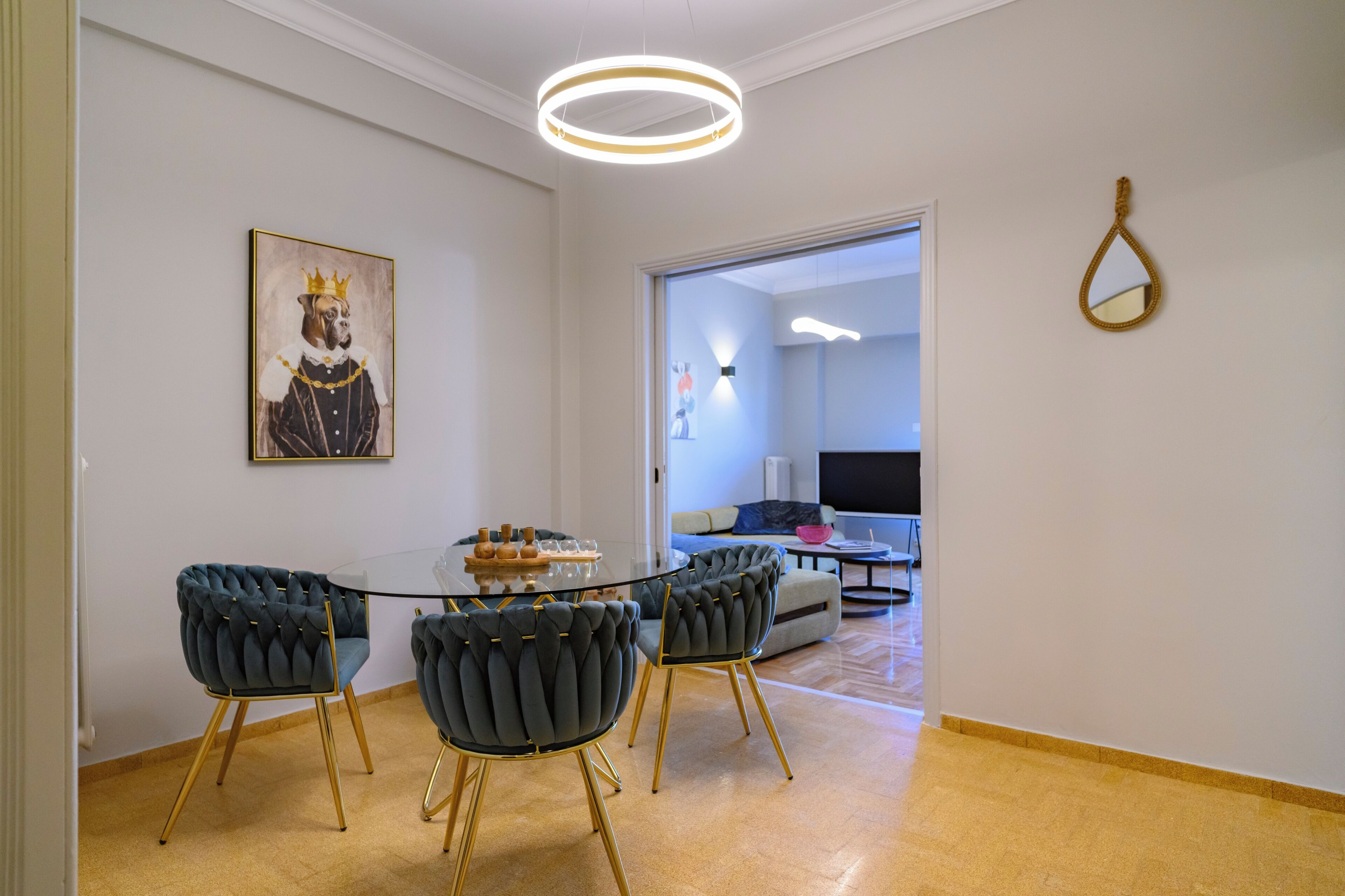 A dining area with a glass table, four upholstered chairs, a framed artwork, and a modern light fixture.