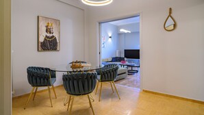 Un comedor con una mesa de vidrio, cuatro sillas tapizadas, una obra de arte enmarcada y una lámpara moderna.