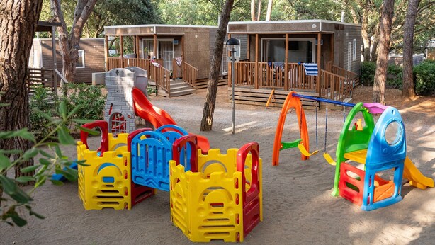 A children's play area with sand, play structures, and wooden cabins in the background. - Mobilhome im Ferienpark mit Grosser Poolanlage (Castiglione della Pescaia)