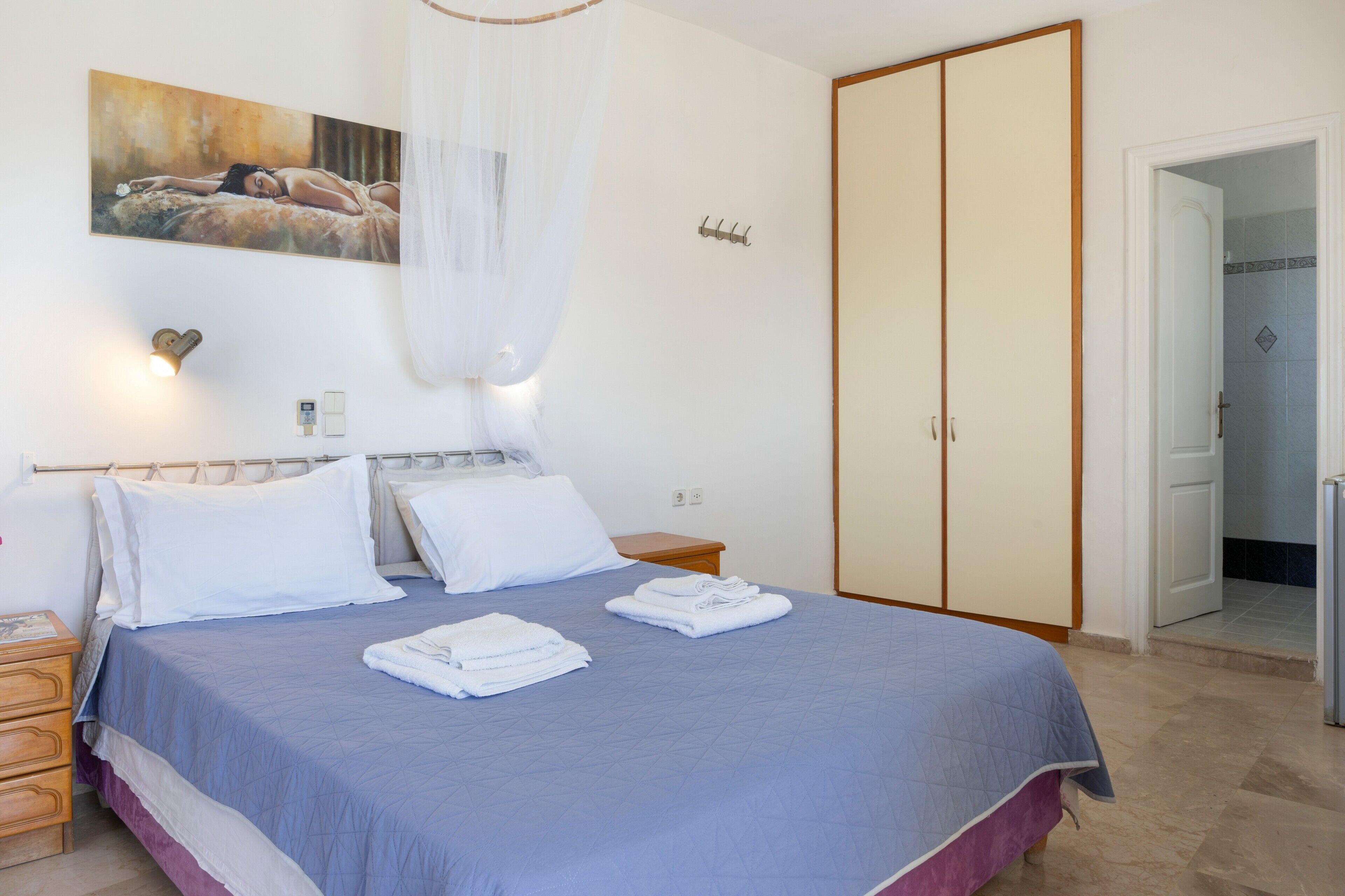 Een slaapkamer met een bed, nachtkastje, kledingkast en een schilderij aan de muur.