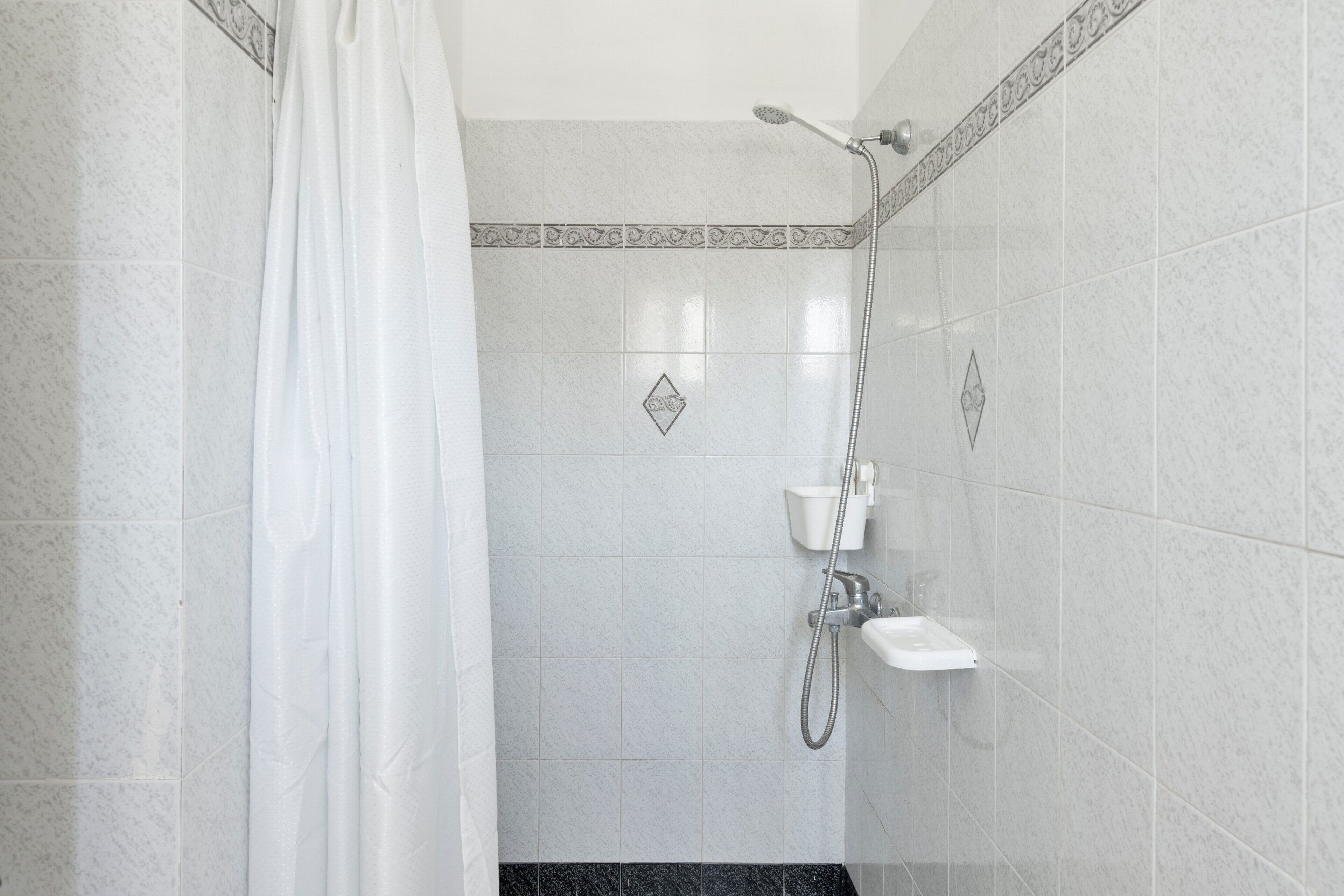 Una ducha con cortina, cabezal de ducha de mano y grifo empotrado en la pared.