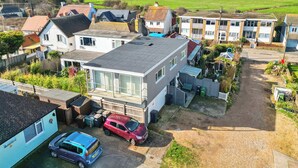 A residential area with houses, a red car, and a blue car parked in front of a building with a large window. - Beachside Coastal Retreat with Ocean Views (Pevensey Bay)