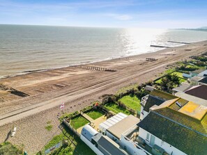 An aerial view of a coastal area with a beach, a promenade, and residential buildings.