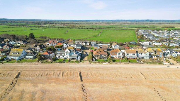 A coastal residential area with houses, a sandy beach, and a green field in the background. - Beachside Coastal Retreat with Ocean Views (Pevensey Bay)