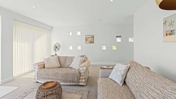 A modern living room with a sofa set, a coffee table, and a woven ottoman.