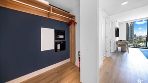 Eine moderne Wohnung mit dunkelblauer Akzentwand, einer Holzwandregal, einem eingebauten schwarzen Stauraum und Blick auf eine Stadtlandschaft durch ein großes Fenster.