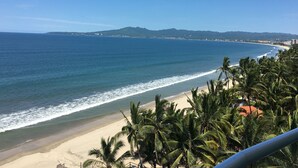 A beach with palm trees, a clear sky, and distant mountains. - Beachfront Condo + Pool - 2 Bedrooms, 2 king beds, 2 baths, w/ AC - Kite Towers (Nuevo Vallarta)