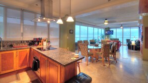 A modern kitchen with granite countertops, wooden cabinets, and a dining area with patterned chairs. - Beachfront Condo + Pool - 2 Bedrooms, 2 king beds, 2 baths, w/ AC - Kite Towers (Nuevo Vallarta)