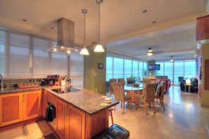 Een moderne keuken met granieten aanrechtbladen, houten keukenkastjes en een eethoek met gestreept beklede stoelen.