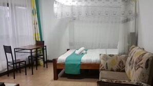 Una habitación con cama, sofá, sillón, mesa y ventana con cortinas.