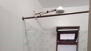 Un área de ducha con puerta de vidrio, una ventana pequeña y un perchero para toallas.