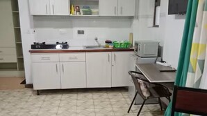 Una cocina compacta con armarios blancos, un microondas y una estufa a gas. Hay una zona de comedor con una mesa y sillas.