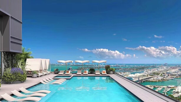 A rooftop infinity pool with lounge chairs and umbrellas, overlooking a cityscape and coastline. - City Views with Bright 1BR Refined in 501 Miami (Miami)