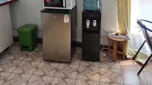 Uma pequena cozinha compacta com micro-ondas, geladeira, dispensador de água e TV fixada na parede.