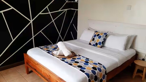 Quarto com cama de madeira, roupa de cama branca e um cobertor colorido com padrão hexagonal.