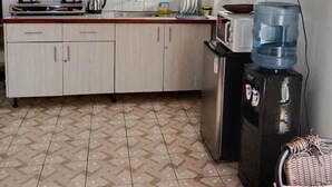 Uma cozinha compacta com armários brancos, fogão a gás, dispenser de água e micro-ondas.