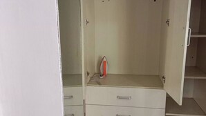 Guarda-roupa branco com duas gavetas e espaço para pendurar, num quarto com soalho em azulejo.