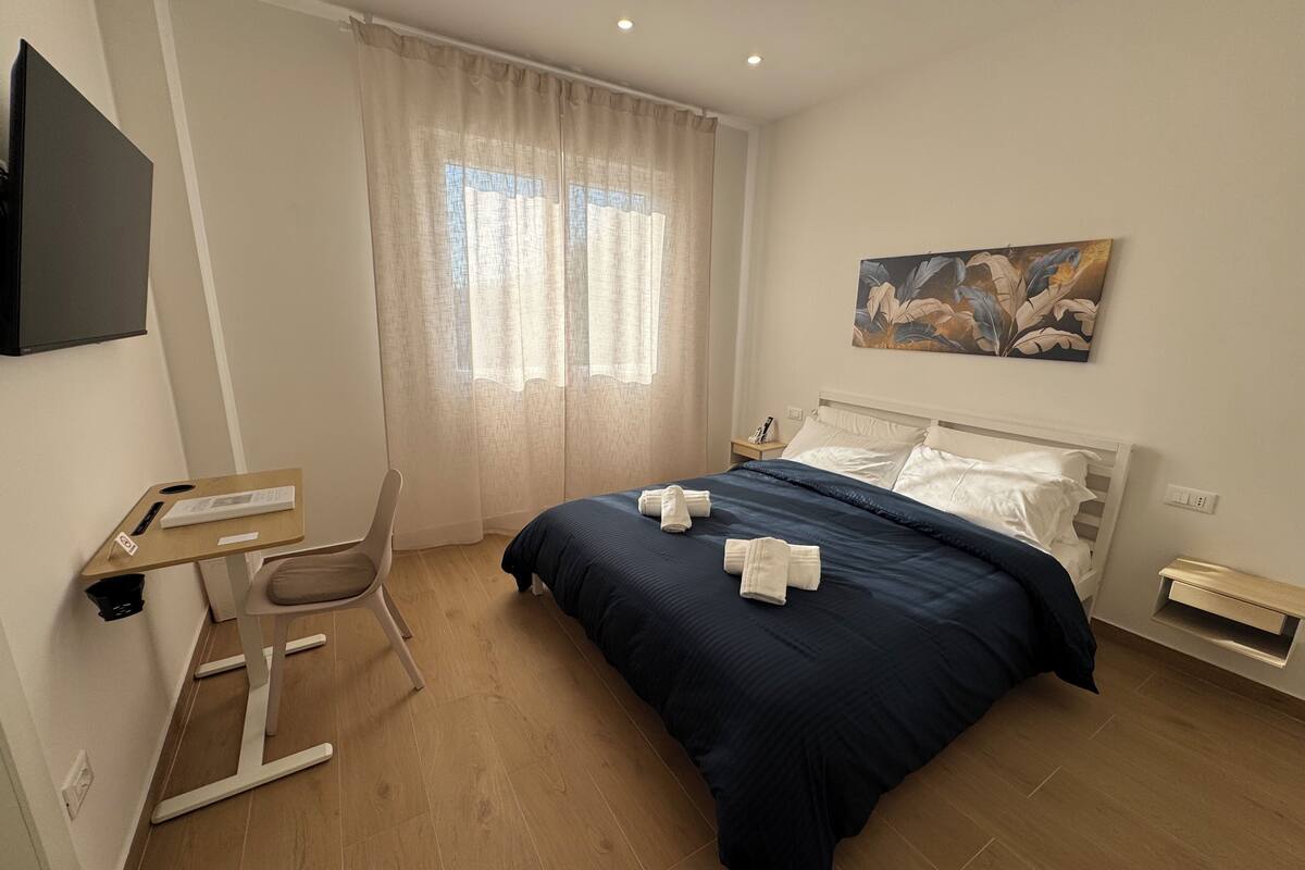 Ein modernes Hotelzimmer mit Bett, Schreibtisch, Stuhl, einem Gemälde und einem fenster mit Vorhängen.
