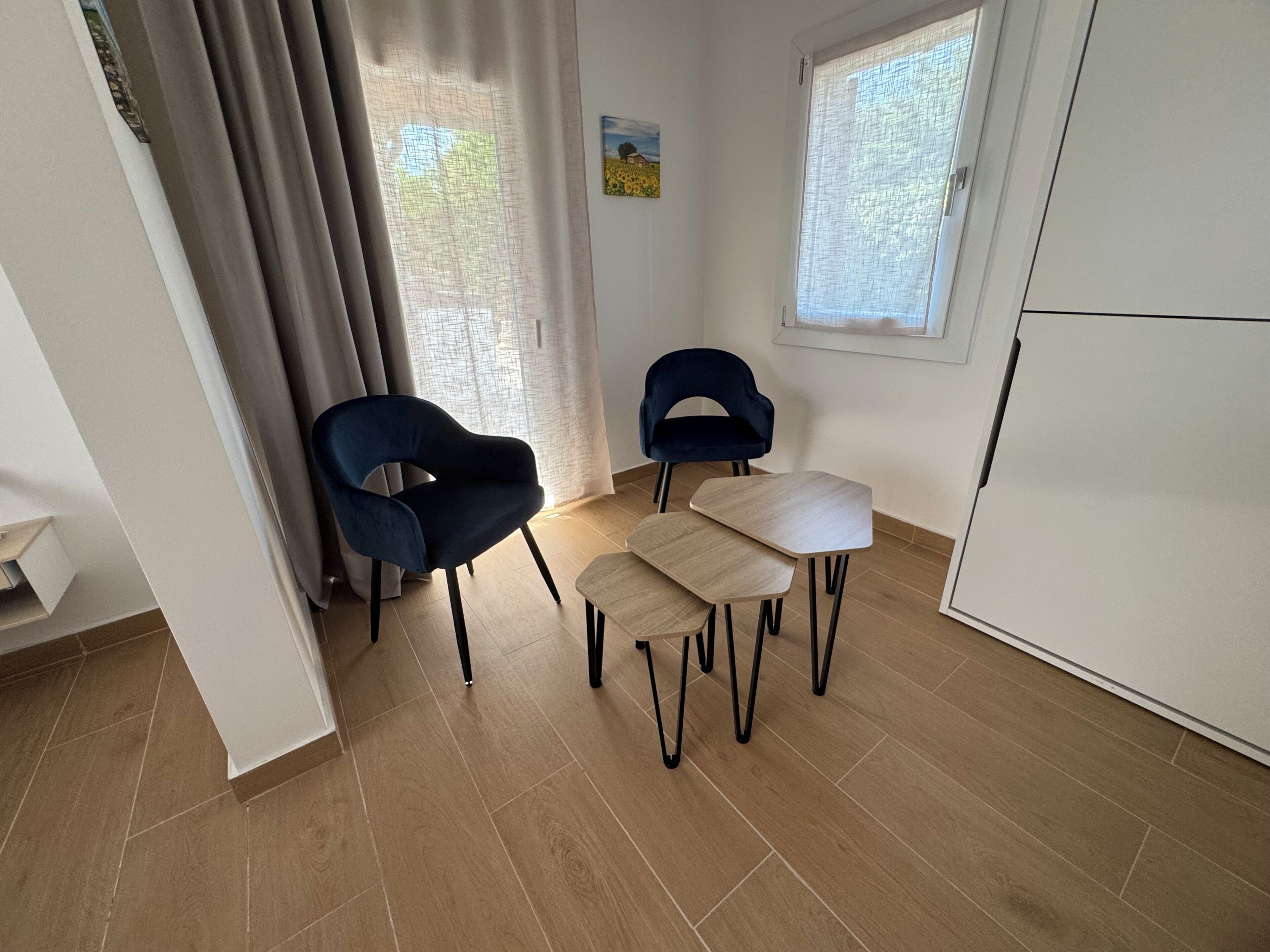 A room with a dining table, two chairs, a cabinet, and a window with curtains.