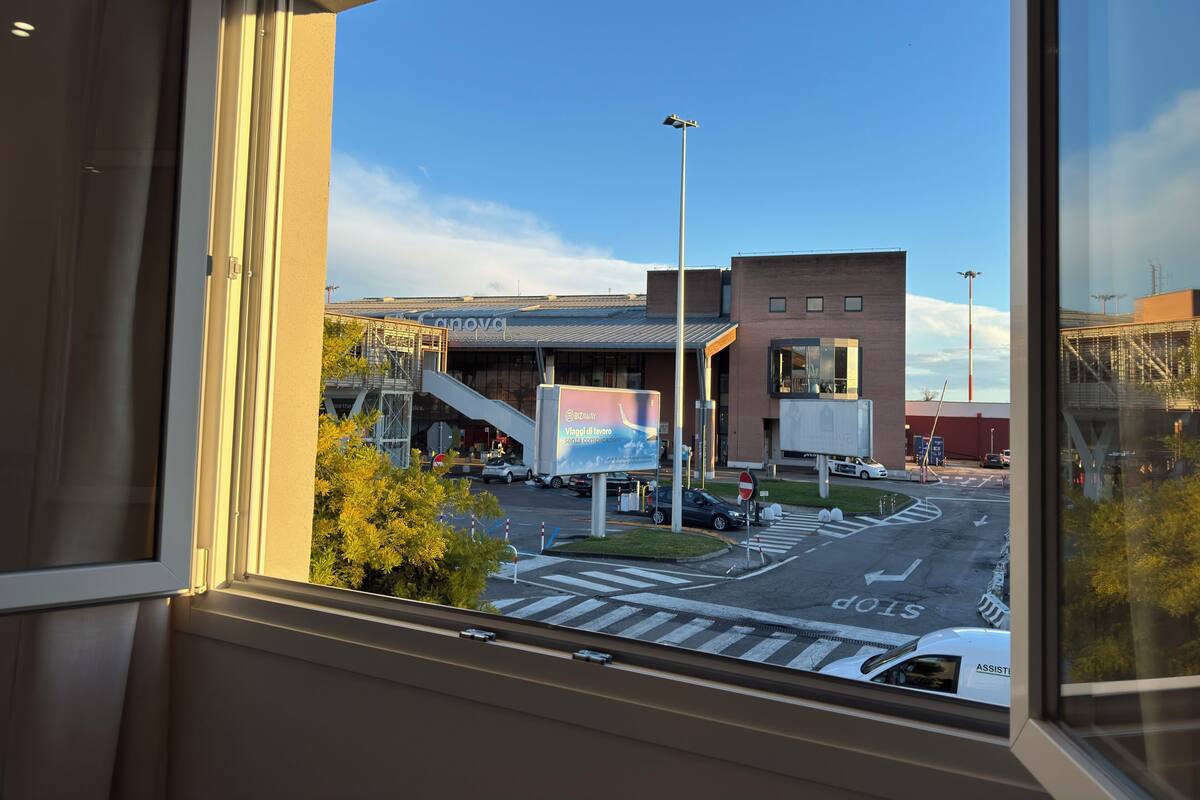 Blick durch ein Fenster eines Gebäudes auf einen klaren Himmel, eine Straße mit Autos und ein Schild.