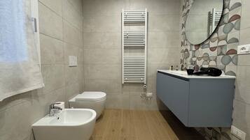 Un baño moderno con bidé, inodoro y lavabo con espejo.